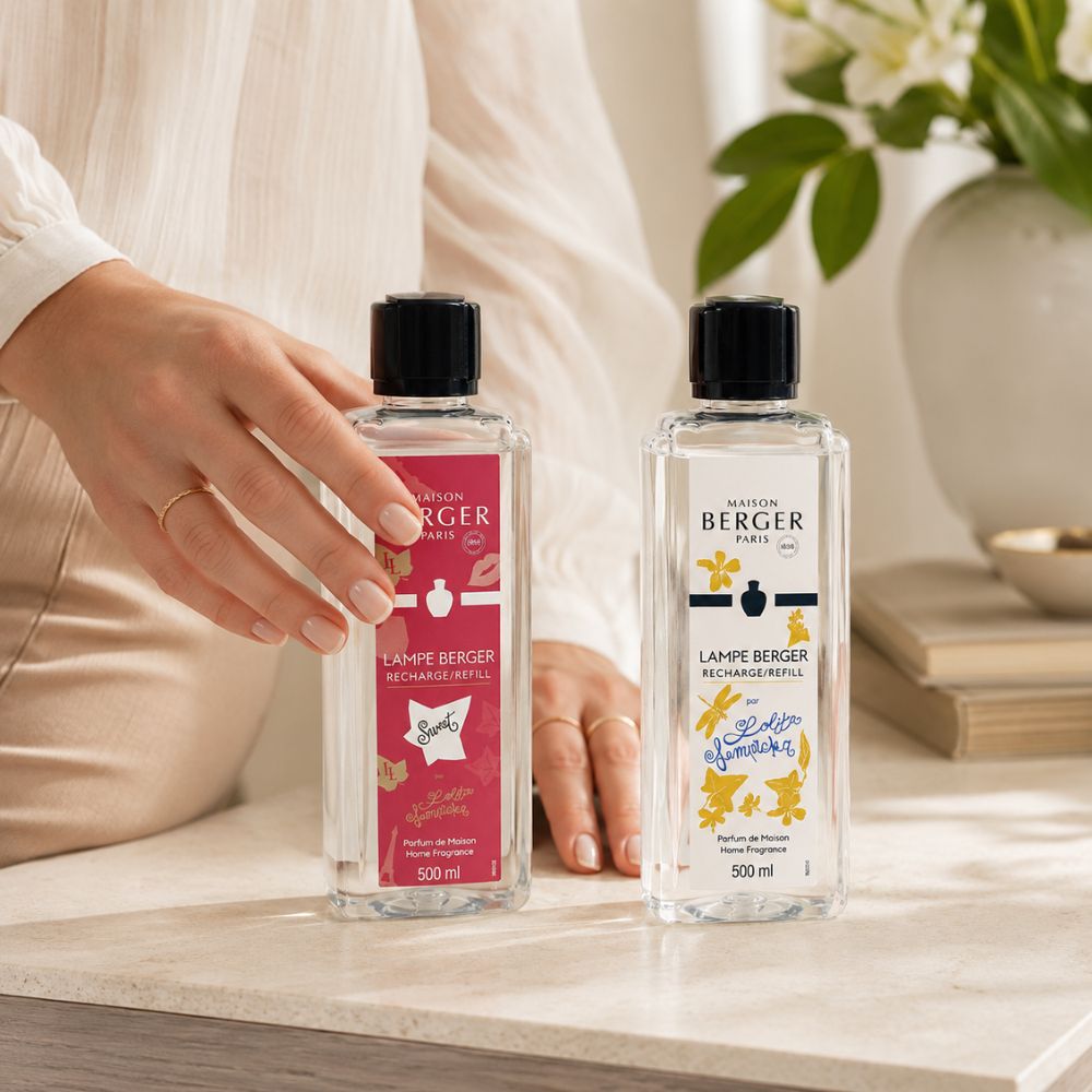 Manos colocando el pack de líquidos dulces para lámpara catalítica Maison Berger Lolita Lempicka Sweet y Lolita Lempicka 500ml sobre mesa con jarrón de flores – D'Arome