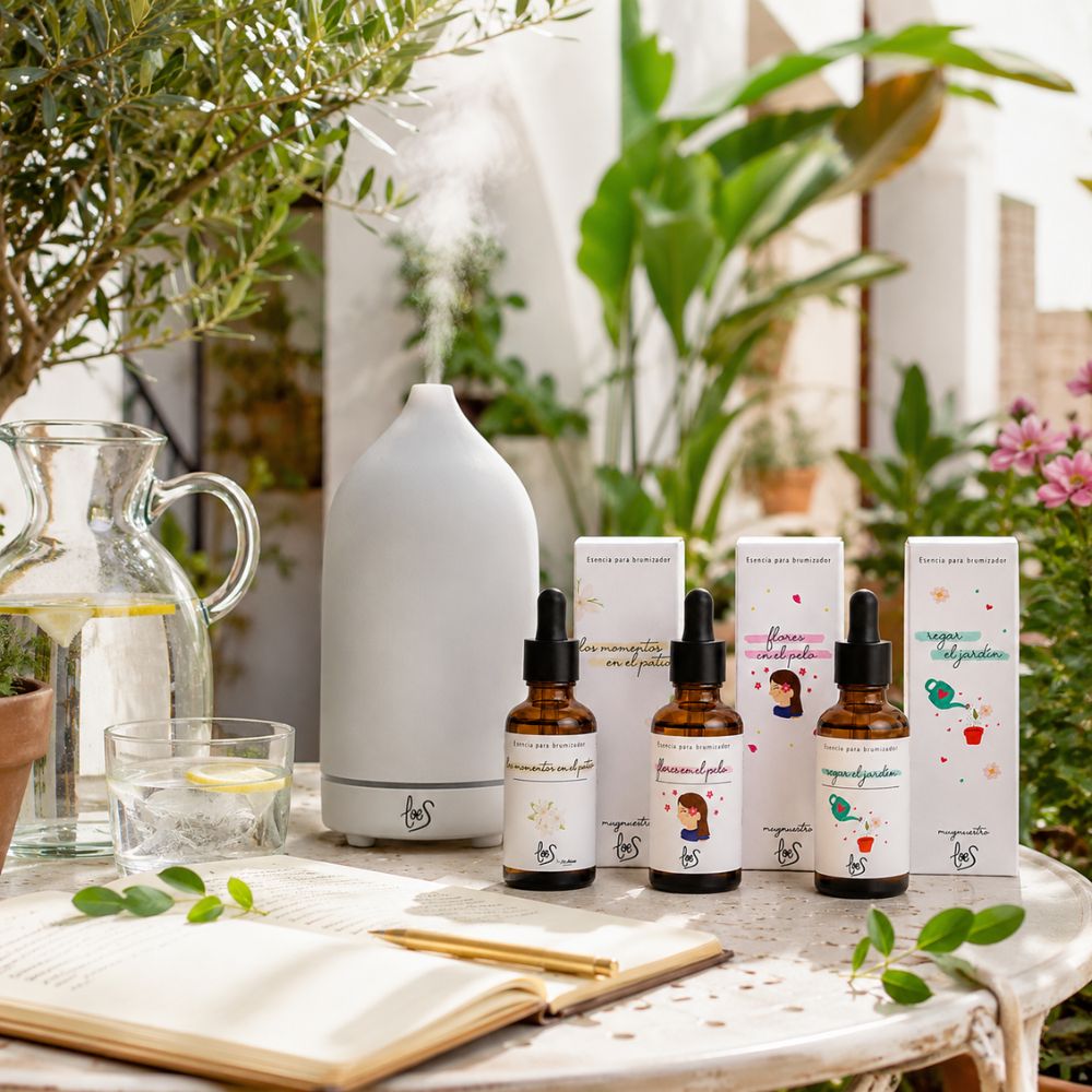Pack tres esencias florales LoeS junto al brumizador cerámico LoeS funcionando en mesa de jardín mediterráneo con olivo y agua con limón – D'Arome