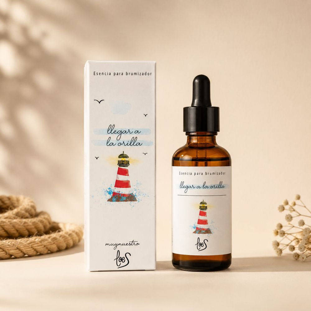 Packshot del envase de la esencia para difusor de aromas "Llegar a la orilla" de LoeS con su caja decorativa ilustrada con faro, sobre fondo crema neutro – D'Arome