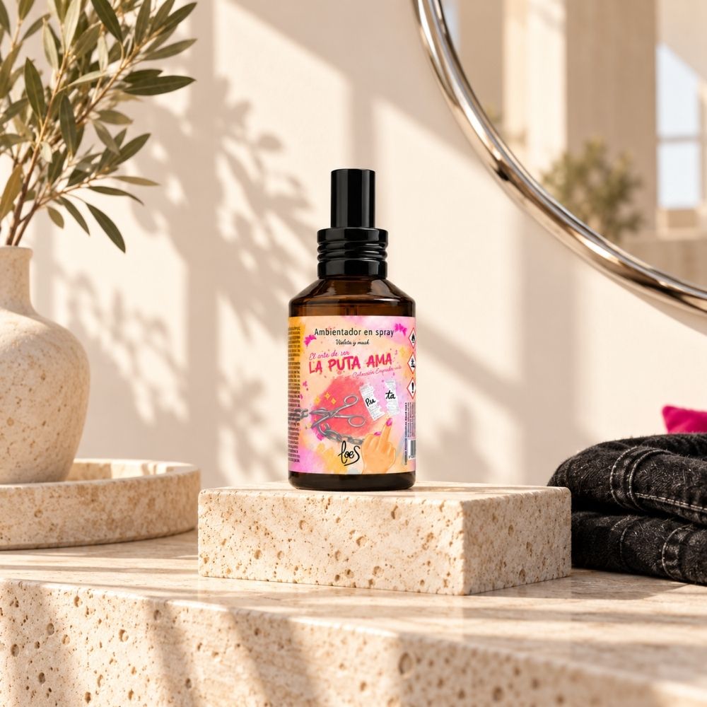 Perfume de ambiente La Puta Ama de LoeS sobre un pedestal de piedra con ramas de olivo y luz natural, colección Empoder-arte – D’Arome