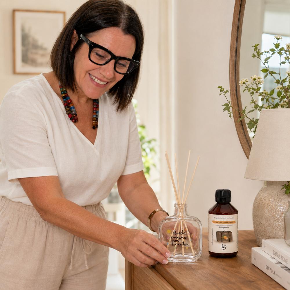 Marí Carmen, CEO de D'Arome, colocando el mikado Nuevos Comienzos LoeS limón y azahar en cómoda de dormitorio con espejo redondo y flores blancas