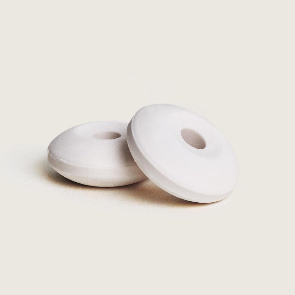 Primer plano de estudio de dos pastillas de cerámica blanca de Maison Berger para difusor de coche con forma de donut.