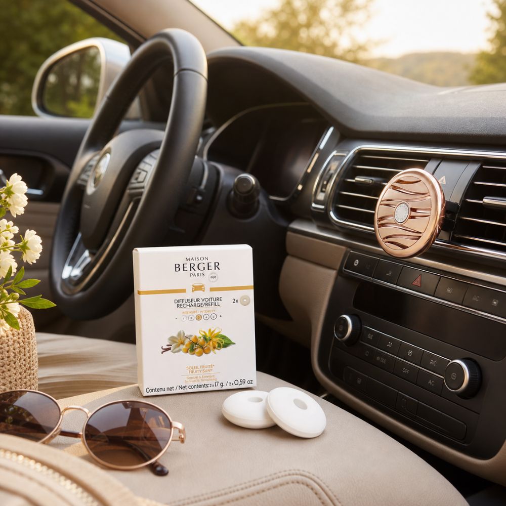 Vista interior de un coche con el difusor Maison Berger de oro rosa en la rejilla y la caja de recargas frutal Soleil Fruité sobre el asiento de cuero beige.