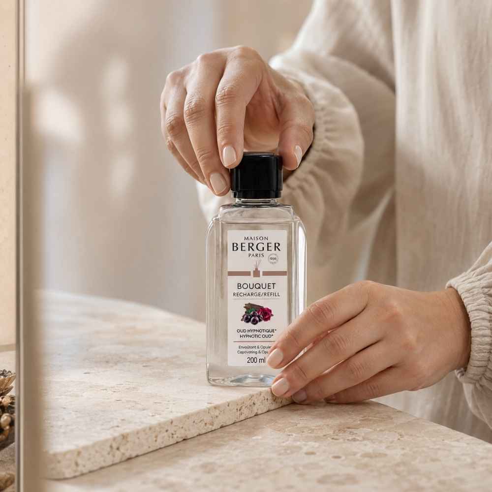 Detalle de manos sosteniendo la recarga de ambientador mikado Oud Hipnótico Maison Berger 200 ml sobre mármol claro – D'Arome
