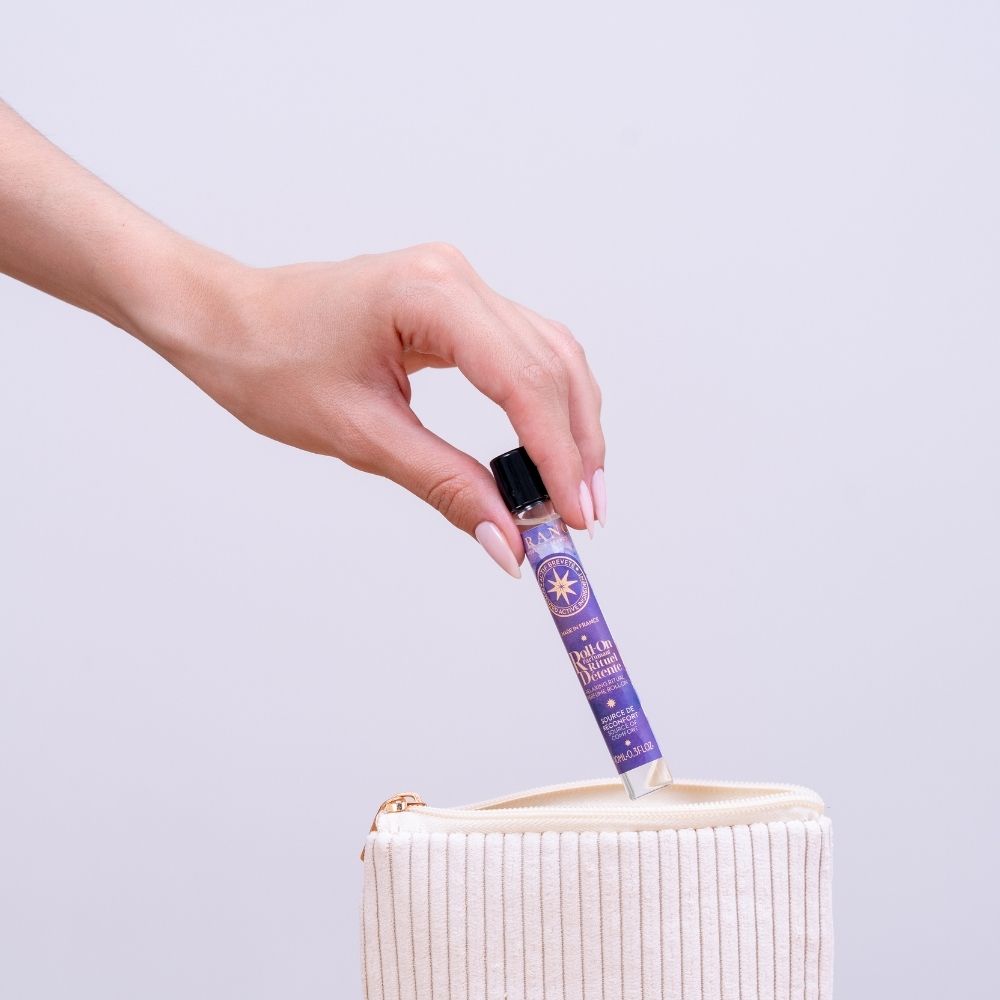 Mano mujer guardando el roll-on perfumado Rituel Détente de Durance en un neceser de viaje de pana beige – D'Arome