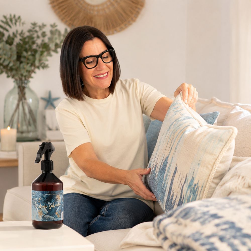 María Carmen, CEO y experta en aromas de D'Arome, perfuma los cojines del sofá con el spray textil Alma Salada de LoeS en un salón de estilo costero – D'Arome