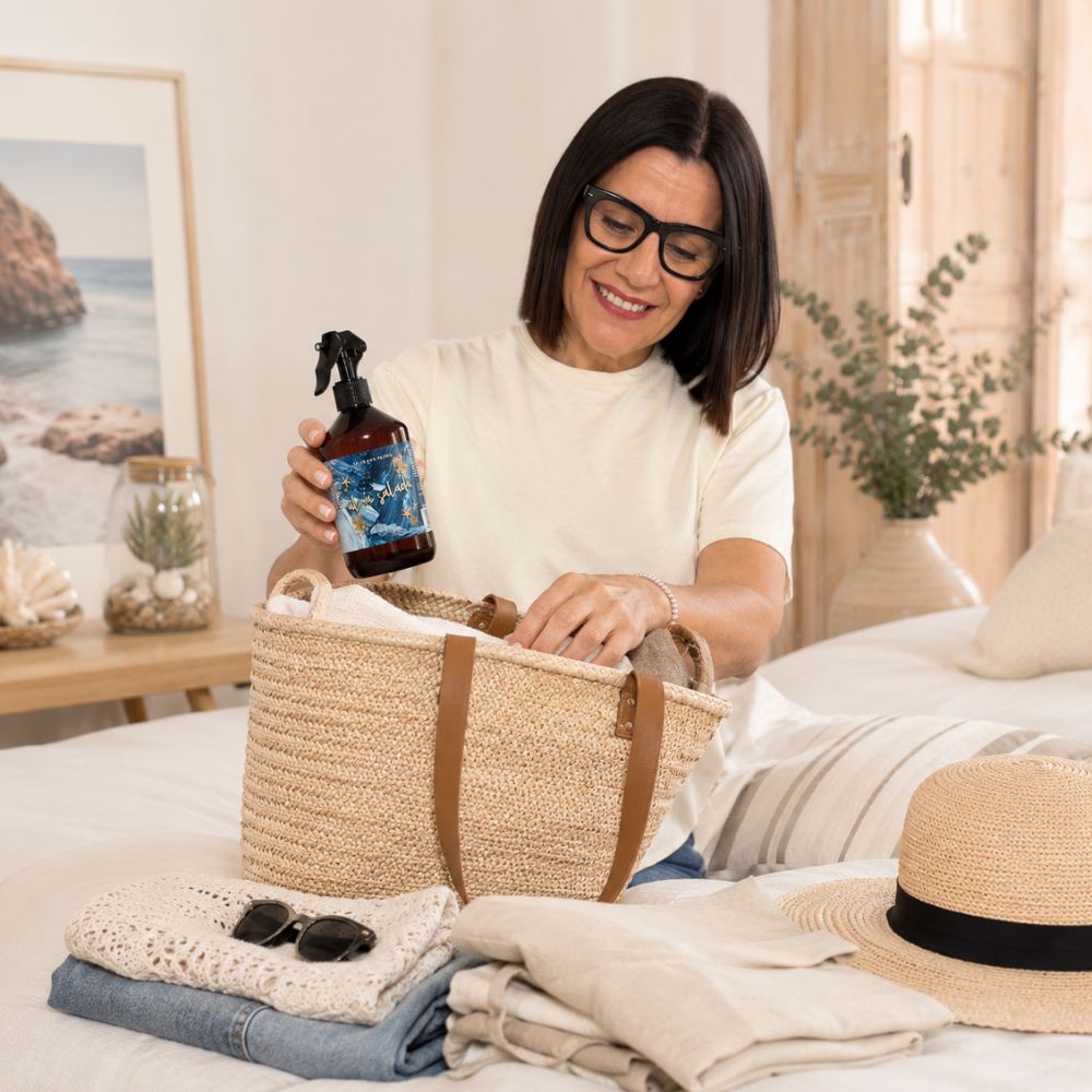 Mari Carmen, CEO y experta en aromas de D'Arome, metiendo el spray textil Alma Salada de LoeS en una cesta de playa   junto a un sombrero de paja – D'Arome