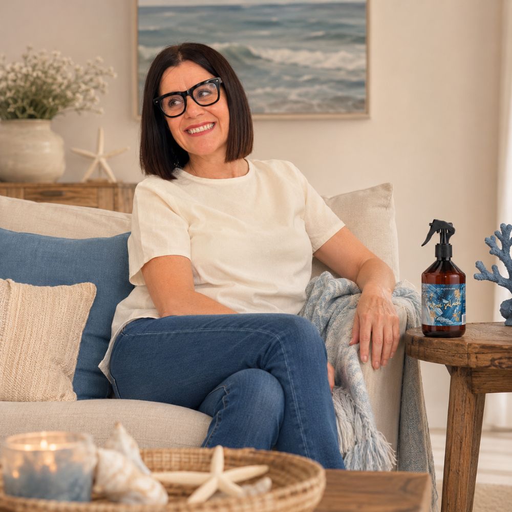 María Carmen, CEO y experta en aromas de D'Arome, en un salón de estilo costero con el spray textil Alma Salada de LoeS y un cuadro de olas del Mediterráneo – D'Arome