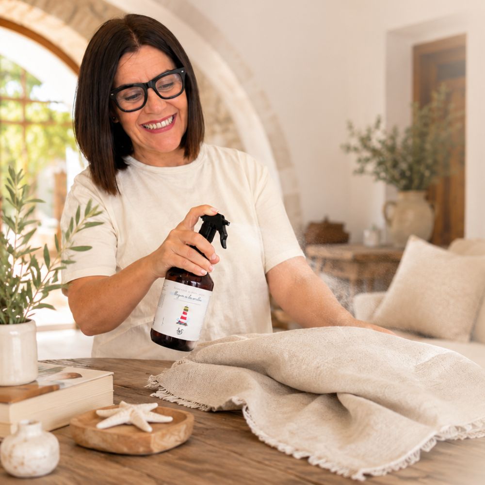 Mari Carmen, CEO y experta en aromas de D'Arome, aplicando spray textil eliminador de olor para tejidos Llegar a la Orilla de LoeS sobre mantel de lino – D'Arome