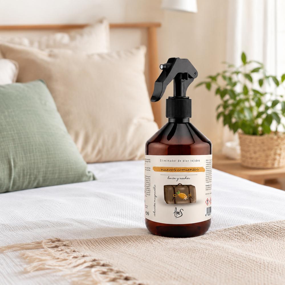 Spray textil eliminador de olores Nuevos Comienzos con aroma a limón y azahar de LoeS sobre cama con cojines en dormitorio natural – D'Arome