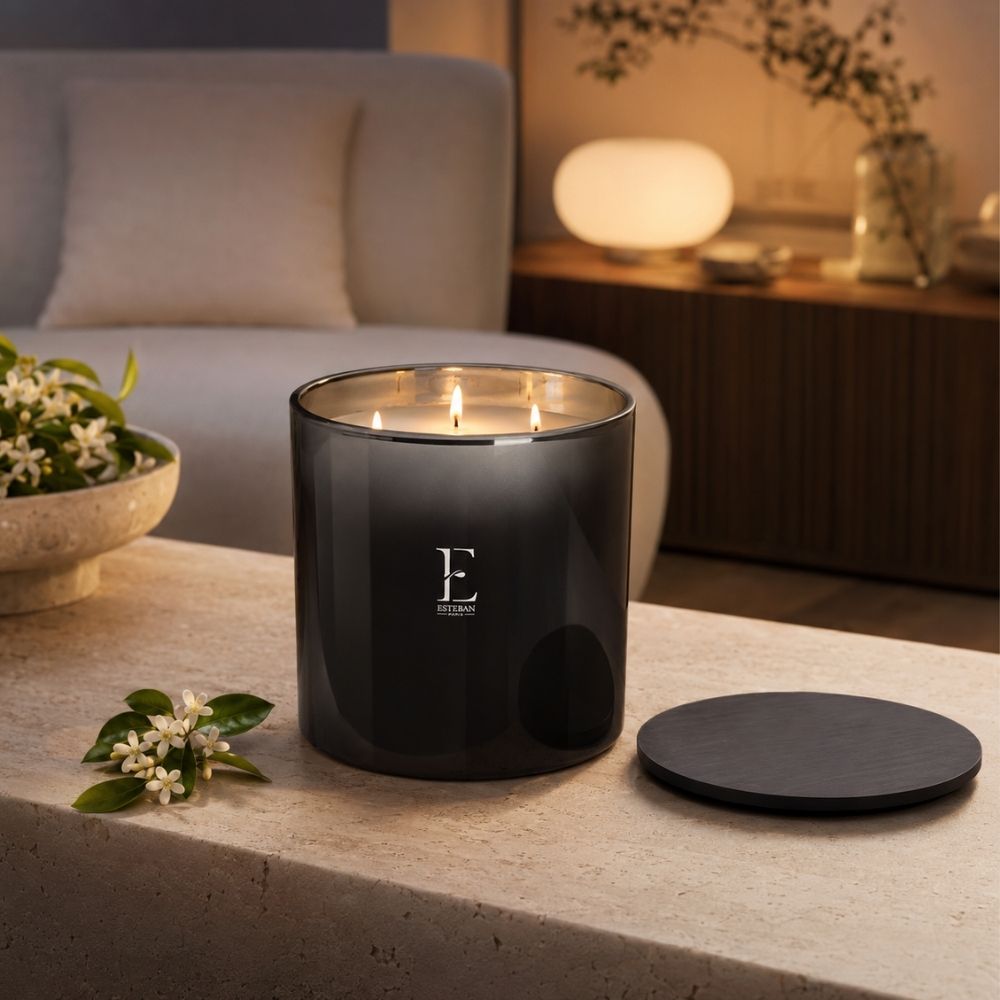 Vela aromática Neroli Edición Premium Esteban París encendida con sus tres mechas en mesa de salón junto a flores de azahar – D'Arome