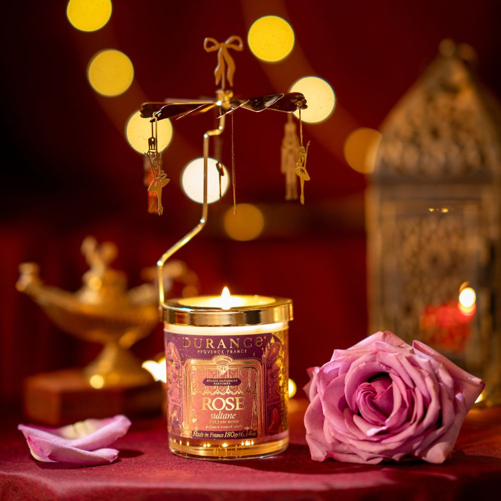 Vela carrusel Rosa Sultana 180gr de Durance encendida junto a rosa fresca y lámpara árabe dorada, con figuras giratorias colgantes de bailarina y cascanueces – D'Arome