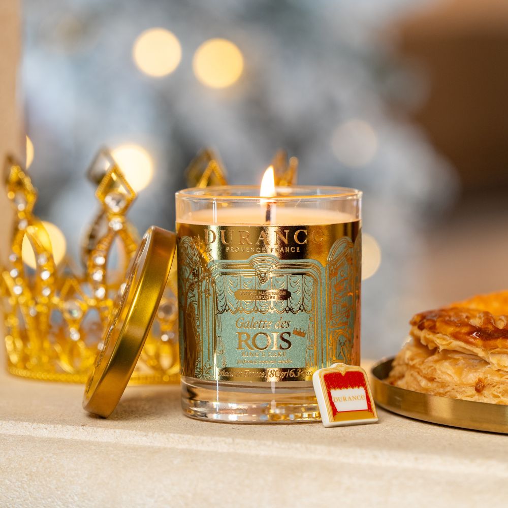 Vela perfumada Pastel de Reyes 180gr de Durance encendida junto a corona dorada y galette des rois, con la haba sorpresa Durance en primer plano – D'Arome